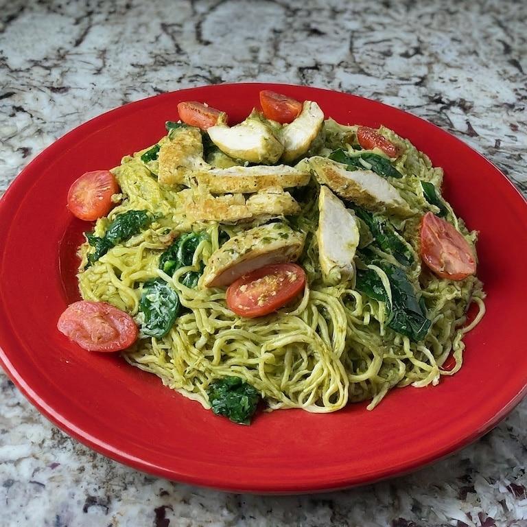 Sliced chicken with pesto sauce, tomatoes and spinach on a red plate.