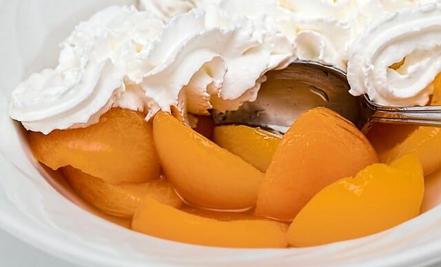 Peaches with whipped cream in a white bowl