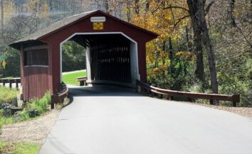 Red wooden covered bridge on a paved road sided by trees.