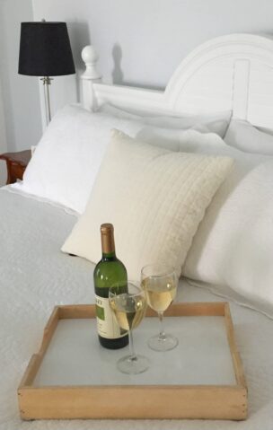 Bed with white linens and a tray holding a bottle of wine and glasses