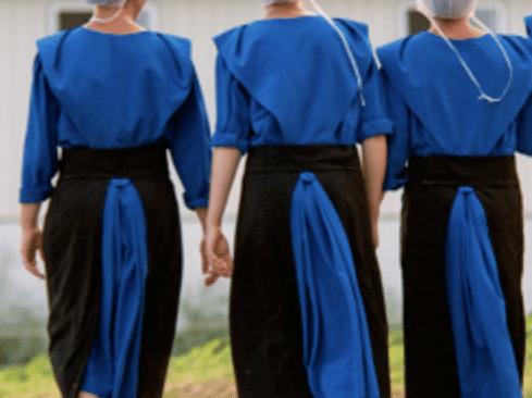 Three amish women in white capes, blue dresses and black aprons.