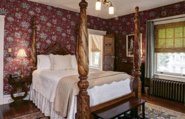 Colonial French large four-poster bed with a white spread and red flowered wallpaper
