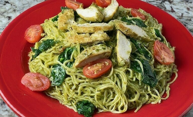 Sliced chicken with pesto sauce, tomatoes and spinach on a red plate.