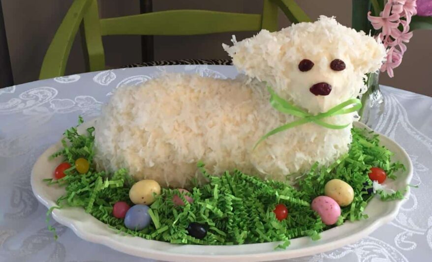 Easter cake shaped like a lamb, on top of green Easter grass with jellybeans.