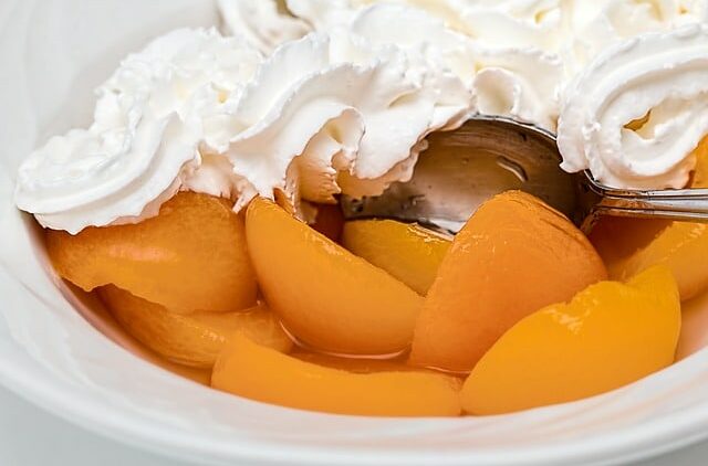 Peaches with whipped cream in a white bowl